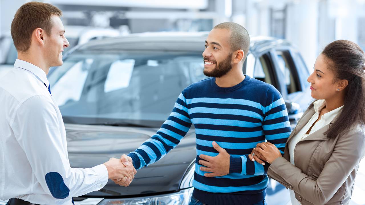 couple-buying-new-car-shaking-hands-with-salesman-at-car-dealership